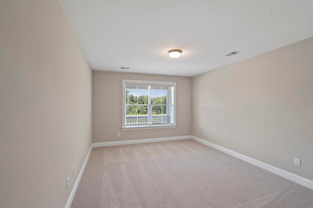 spare room featuring light colored carpet, visible vents, and baseboards