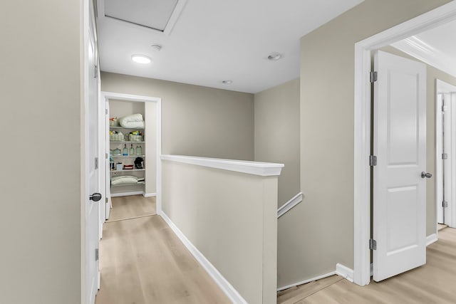 hallway featuring baseboards, attic access, light wood-style flooring, and an upstairs landing