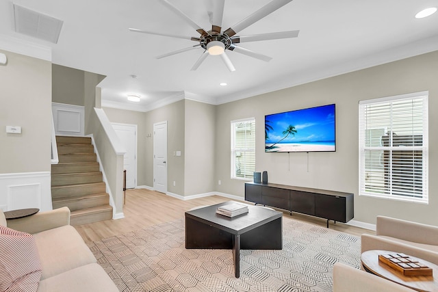 living room with visible vents, crown molding, light wood-style floors, ceiling fan, and stairway