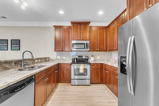 kitchen featuring light stone countertops, a sink, light wood-style flooring, stainless steel appliances, and ornamental molding