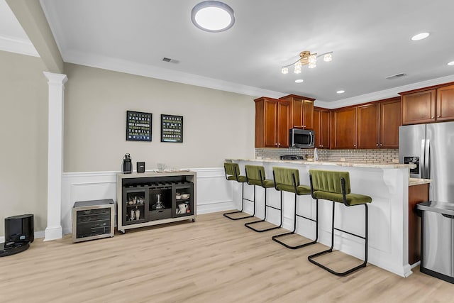 kitchen featuring appliances with stainless steel finishes, a kitchen bar, light wood-type flooring, visible vents, and ornamental molding