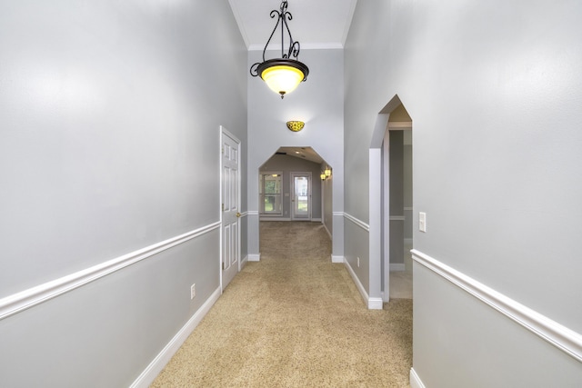 hall featuring crown molding, baseboards, arched walkways, and light colored carpet