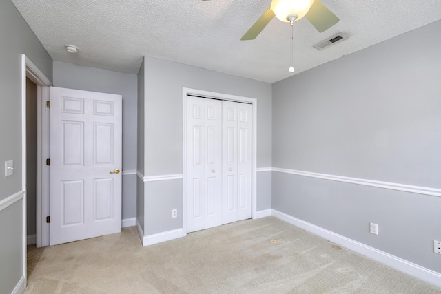 unfurnished bedroom with a textured ceiling, a closet, visible vents, light carpet, and baseboards
