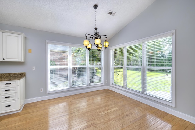 unfurnished dining area with light wood-style flooring, a textured ceiling, visible vents, a chandelier, and lofted ceiling