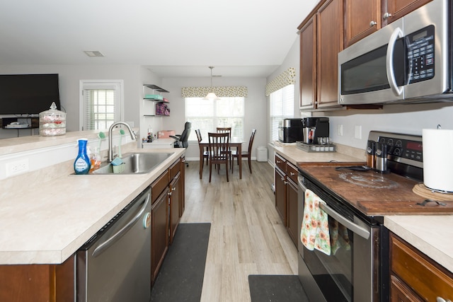 kitchen with an inviting chandelier, appliances with stainless steel finishes, light hardwood / wood-style flooring, pendant lighting, and sink