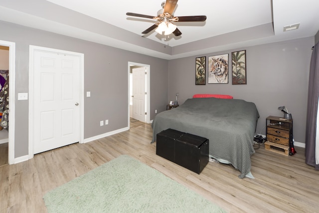 bedroom with a raised ceiling, light hardwood / wood-style floors, a closet, and ceiling fan