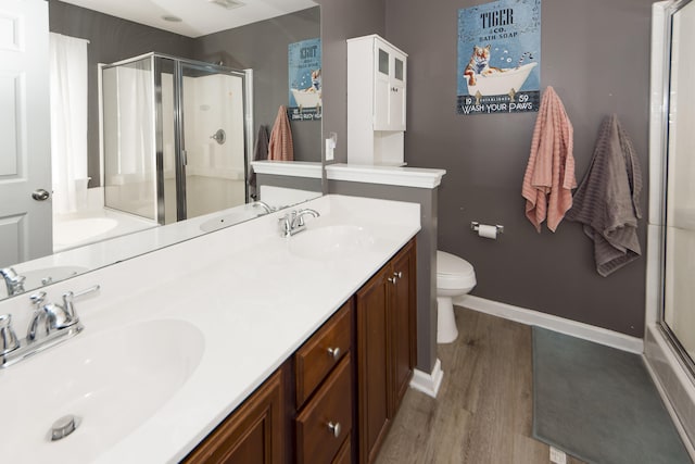 bathroom with double sink, wood-type flooring, a shower with door, toilet, and oversized vanity