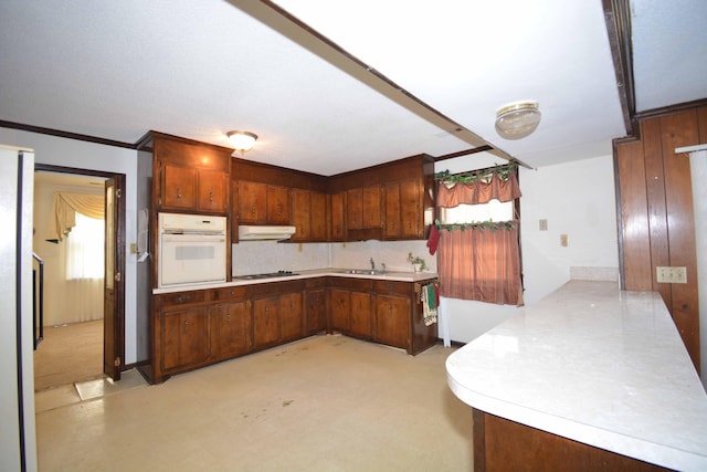 kitchen featuring kitchen peninsula, ornamental molding, cooktop, sink, and oven