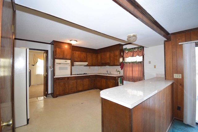 kitchen featuring wood walls, white appliances, sink, ornamental molding, and kitchen peninsula