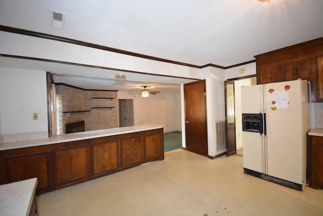 kitchen with ceiling fan, a large fireplace, white fridge with ice dispenser, a textured ceiling, and ornamental molding