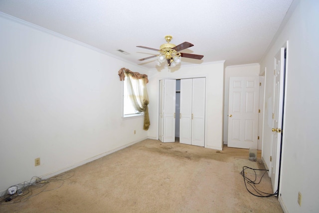 unfurnished bedroom featuring ceiling fan, light colored carpet, a textured ceiling, a closet, and ornamental molding