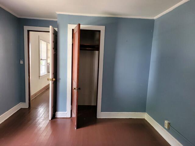 unfurnished bedroom featuring baseboards, a closet, ornamental molding, and dark wood-style flooring