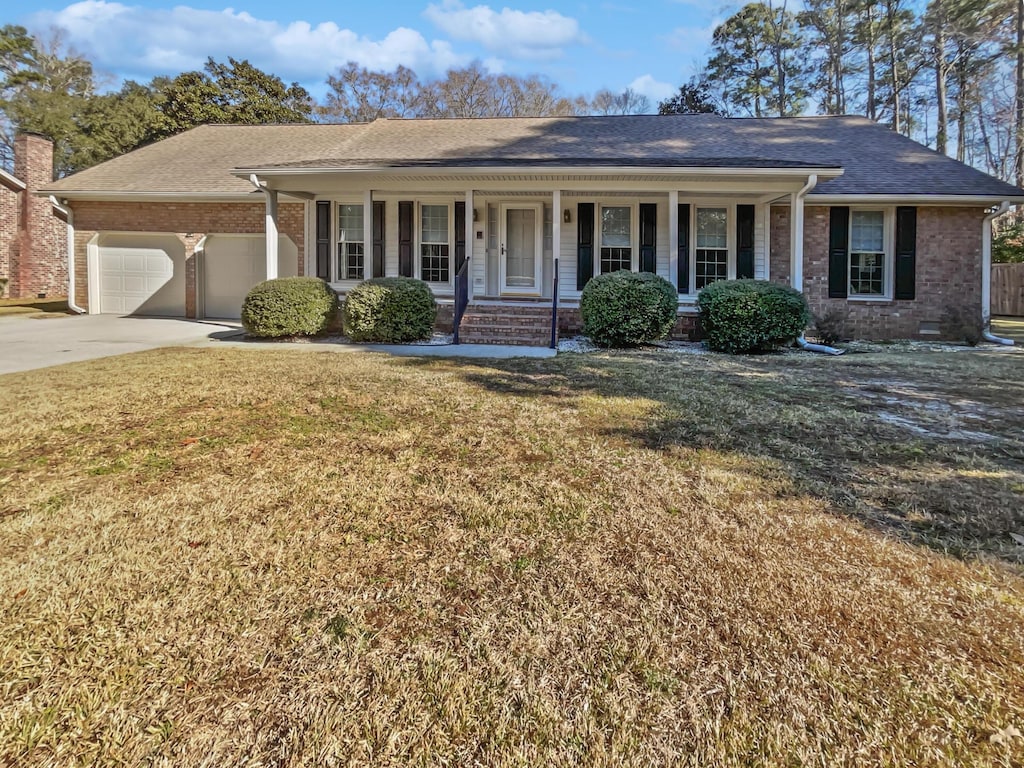 ranch-style house featuring a garage, covered porch, and a front lawn