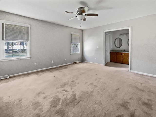 unfurnished bedroom with ceiling fan, connected bathroom, light carpet, and multiple windows