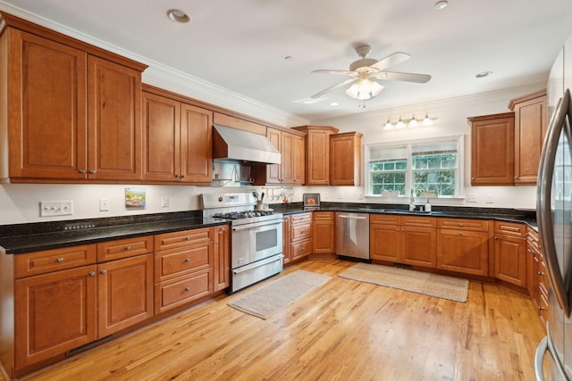 kitchen with light wood-type flooring, brown cabinetry, wall chimney exhaust hood, and stainless steel appliances