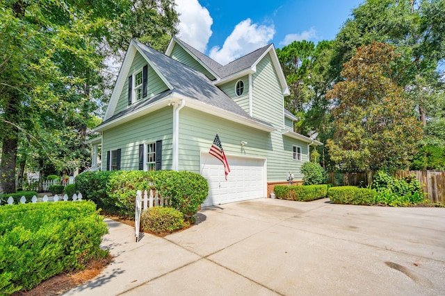 view of property exterior featuring concrete driveway, a shingled roof, and fence