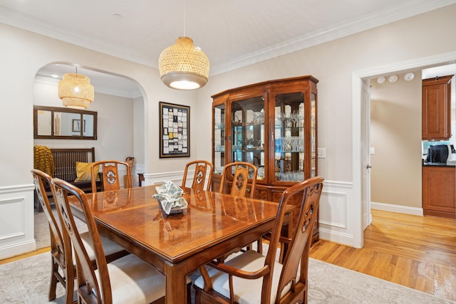 dining room featuring arched walkways, wainscoting, ornamental molding, light wood-type flooring, and a decorative wall