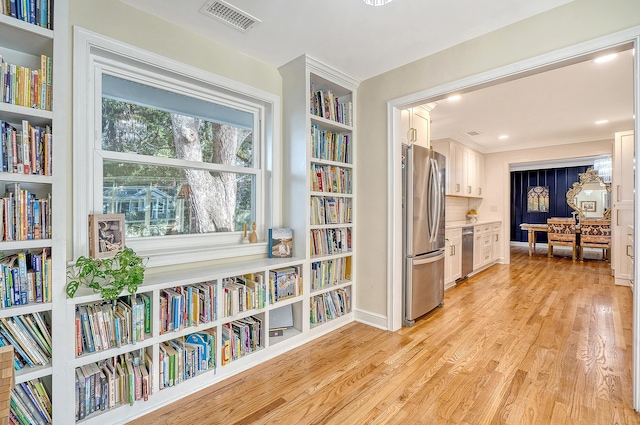 living area with bookshelves, light wood finished floors, and visible vents