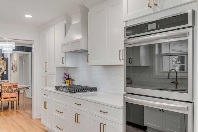 kitchen with stainless steel appliances, light countertops, white cabinets, and custom range hood