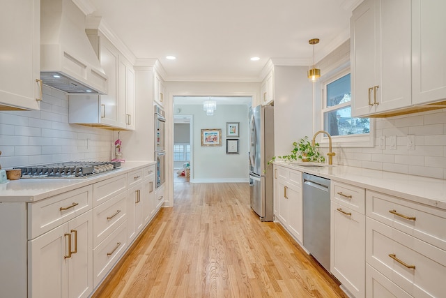 kitchen with a sink, white cabinets, appliances with stainless steel finishes, custom exhaust hood, and light wood finished floors