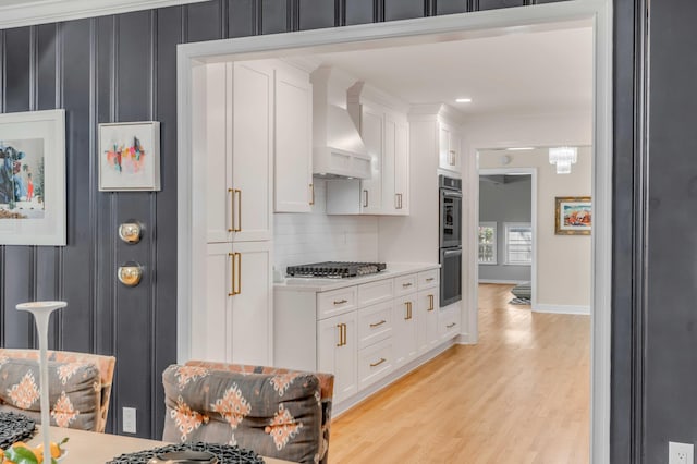 kitchen with light countertops, light wood-style flooring, appliances with stainless steel finishes, white cabinetry, and wall chimney exhaust hood