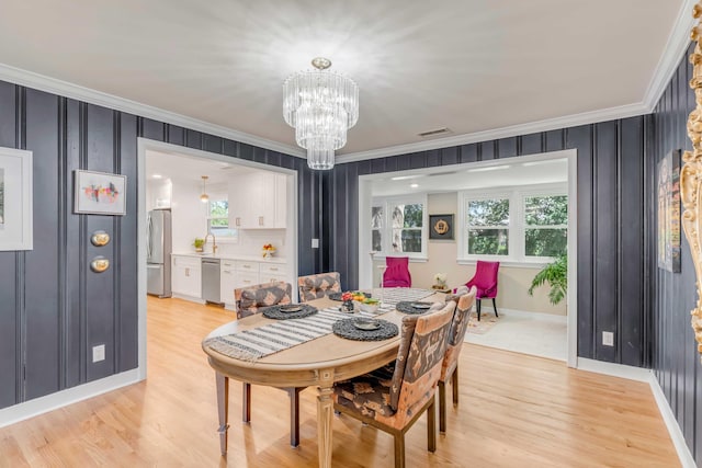 dining room with a notable chandelier, light wood-style flooring, visible vents, and crown molding