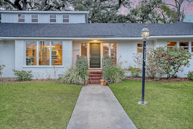 view of front of property with roof with shingles, a front lawn, and brick siding