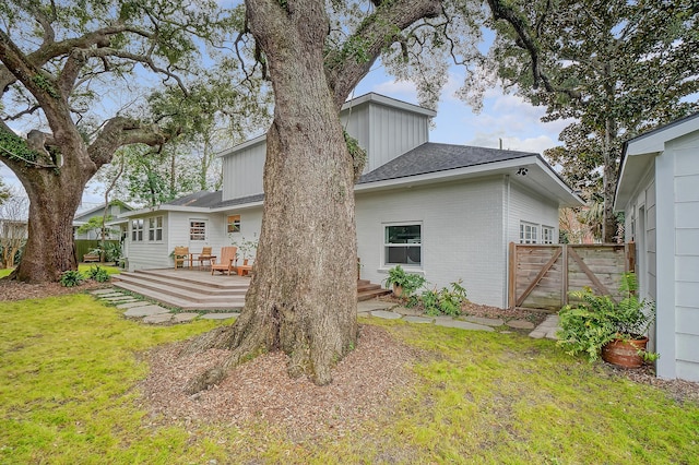 rear view of property with brick siding, fence, a deck, and a lawn