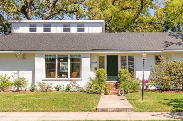 view of front of house featuring a shingled roof, a front yard, brick siding, and board and batten siding