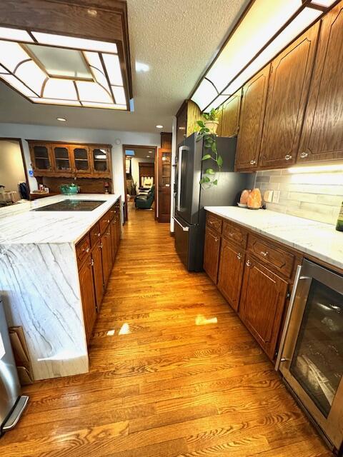 kitchen featuring stainless steel fridge, a textured ceiling, black electric cooktop, light hardwood / wood-style floors, and wine cooler