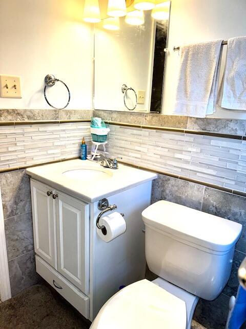 bathroom featuring tasteful backsplash, vanity, tile walls, and toilet