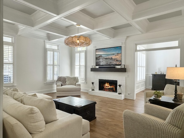 living area with a wealth of natural light, beam ceiling, a brick fireplace, and wood finished floors