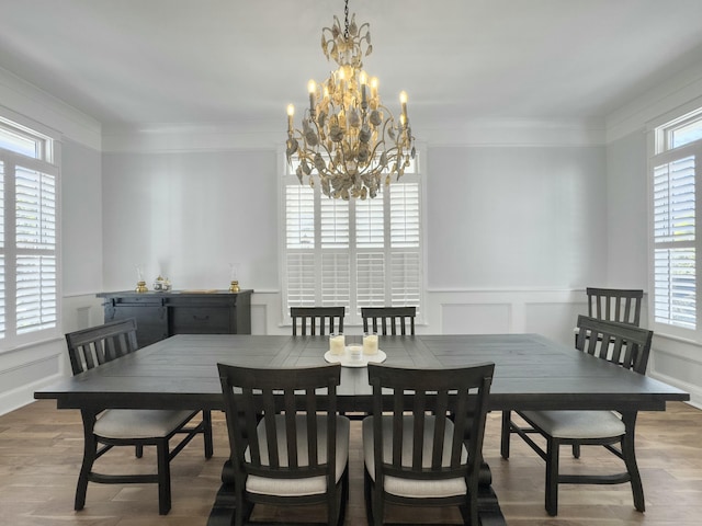 dining area featuring crown molding, a decorative wall, wood finished floors, and a chandelier