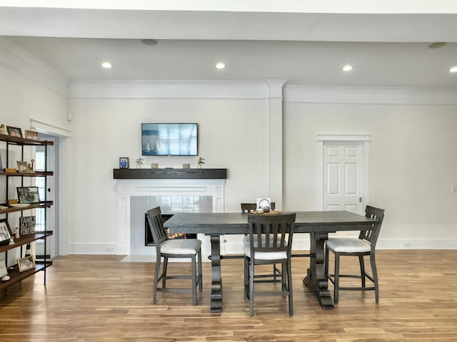 dining space featuring wood finished floors, baseboards, recessed lighting, a fireplace, and ornamental molding