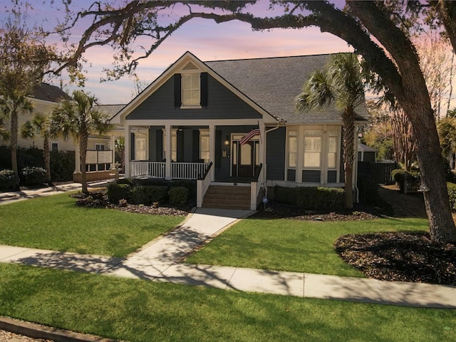 view of front of home with a porch, a lawn, and roof with shingles