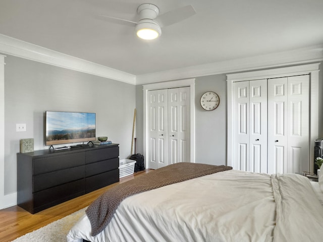 bedroom featuring ornamental molding, two closets, a ceiling fan, and wood finished floors