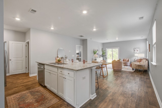 kitchen with light stone countertops, a kitchen island with sink, dark hardwood / wood-style flooring, white cabinetry, and a kitchen bar