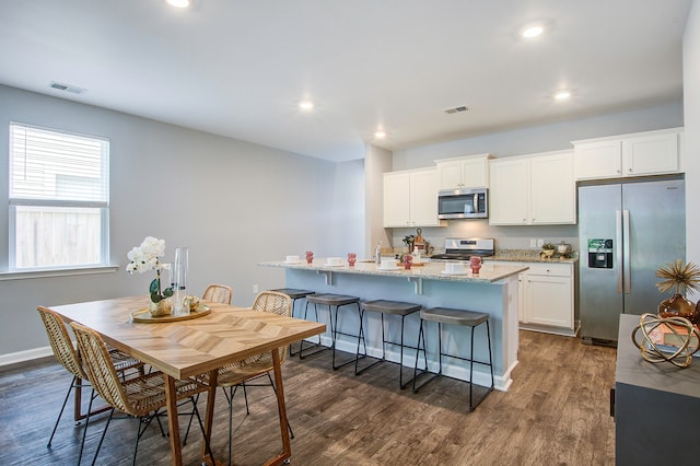 kitchen with a kitchen island with sink, a breakfast bar area, dark hardwood / wood-style flooring, appliances with stainless steel finishes, and white cabinetry