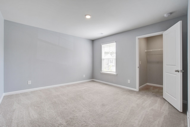 unfurnished bedroom with a closet, a walk in closet, and light carpet