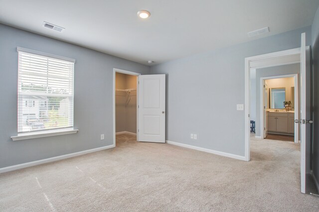 unfurnished bedroom featuring a closet, a walk in closet, and light carpet