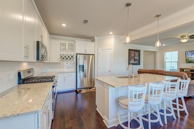 kitchen featuring decorative light fixtures, white cabinetry, sink, stainless steel appliances, and a center island with sink