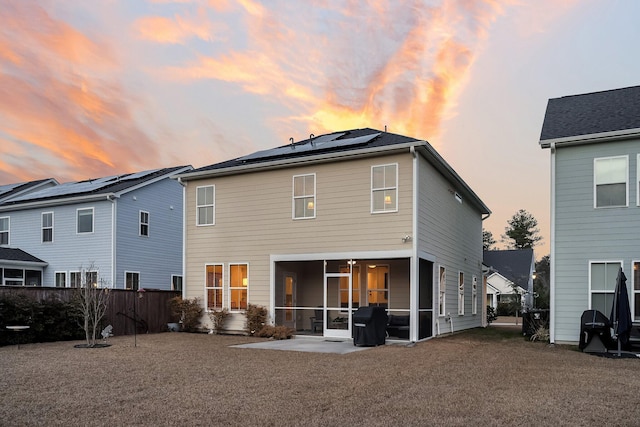 back house at dusk with a patio area, a sunroom, and solar panels