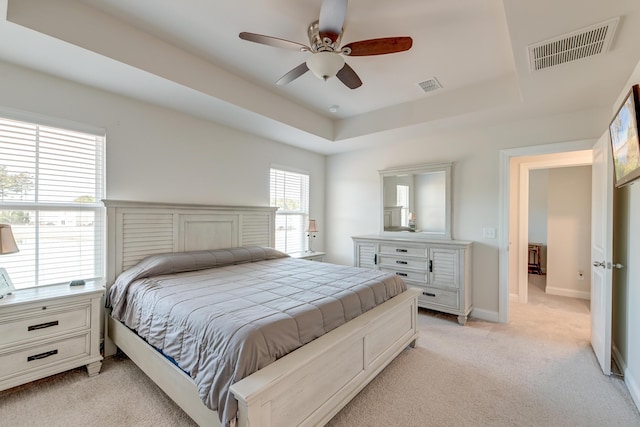 bedroom featuring a raised ceiling, light colored carpet, and ceiling fan