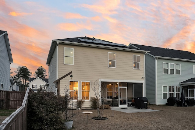 back house at dusk featuring a patio area, a sunroom, and solar panels