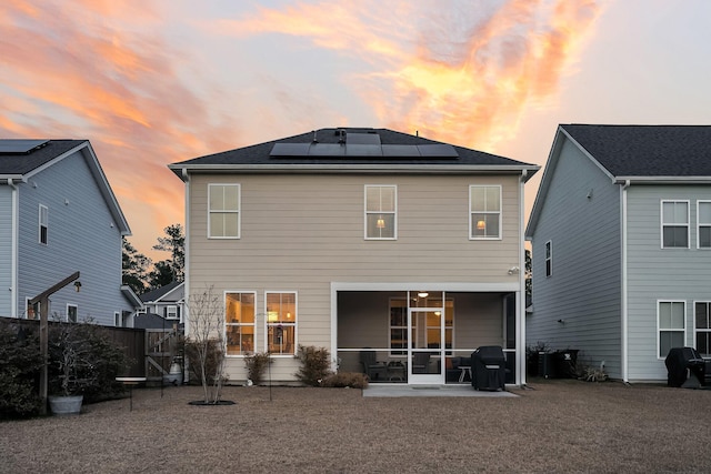 back house at dusk with a patio, a sunroom, and solar panels