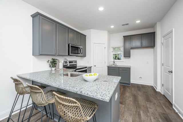 kitchen featuring light stone counters, gray cabinetry, dark hardwood / wood-style flooring, appliances with stainless steel finishes, and a kitchen breakfast bar