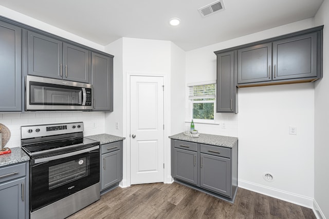 kitchen with light stone counters, stainless steel appliances, tasteful backsplash, dark hardwood / wood-style flooring, and gray cabinets