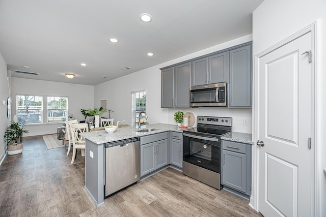 kitchen featuring stainless steel appliances, kitchen peninsula, light stone countertops, and light hardwood / wood-style flooring