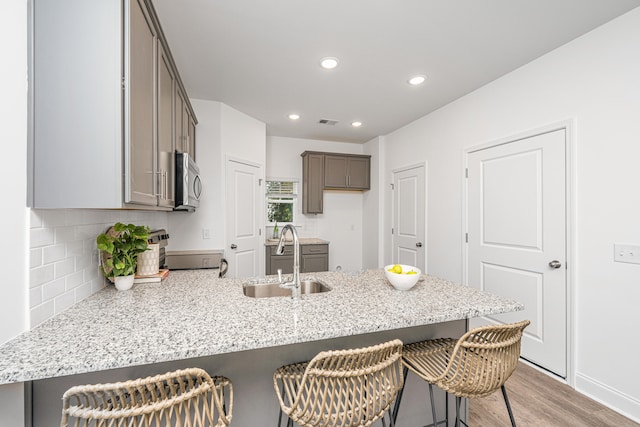 kitchen with light wood-type flooring, range, sink, kitchen peninsula, and a kitchen bar