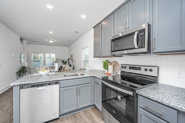 kitchen featuring sink, kitchen peninsula, appliances with stainless steel finishes, light stone countertops, and light hardwood / wood-style floors